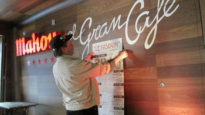 El artista Juan Rafael colocando uno de los carteles hechos a mano en El Gran Café. © Fotografía: E. Otero.
