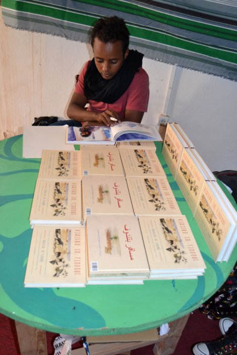 Joven saharaui muestra al público el libro del pintor Javier de Blas "Viajero en Tindouf". ARTifariti 2015. Fotografía: Antonio Muñoz.